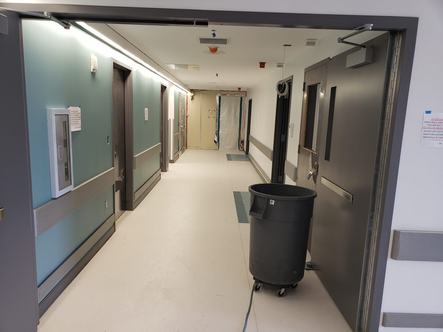 A hallway with two doors and a trash can.
